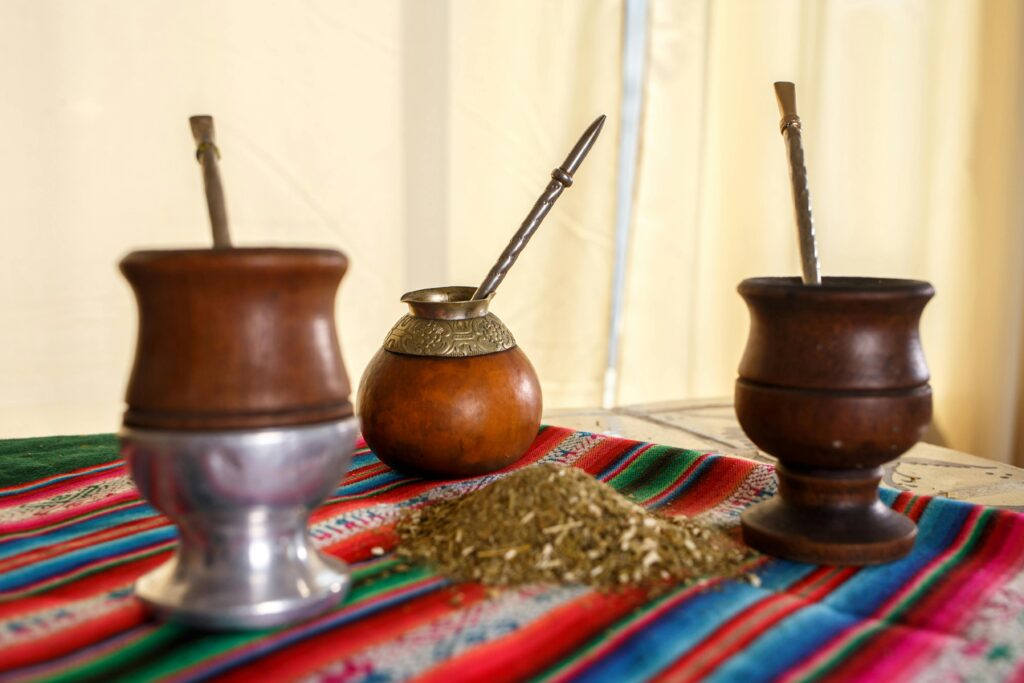 Three traditional yerba mate cups with bombillas on a vibrant cloth indoors.